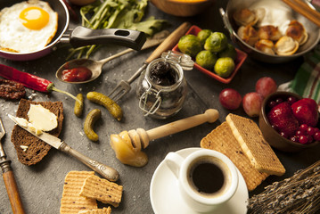 Table with food in breakfast or lunch: omelette, cabbage, oil, chili, ketchup, arugula, onion, garlic, noodles, cucumber, coffee, biscuits, orange, bread and butter