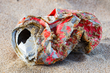 bunched up old red tin can lies in the sand on the beach