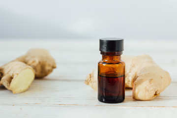 Ginger essential oil in glass bottle with ginger root behind.