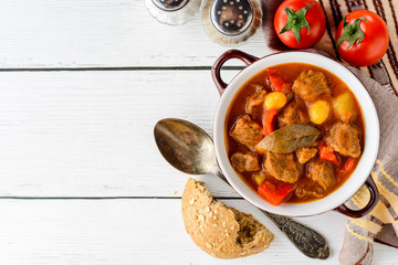 Goulash in ceramic bowl on white wooden background. Traditional hungarian soup.