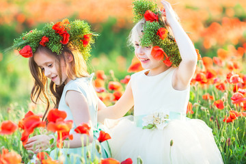 little girl model, poppies, summer fashion concept - close-up on girly games in the field of poppies, two girlfriends hugging. happy, smiling cute princeses with a wreath of fresh poppy.