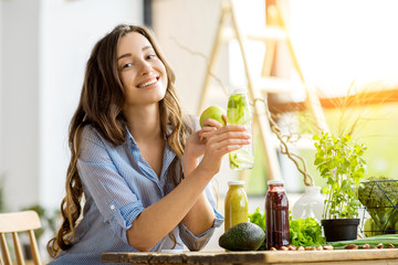 Beautiful happy woman sitting with drinks and healthy green food at home. Vegan meal and detox concept