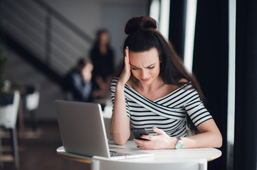 Portrait of stressed office young woman holding a cellphone in hands in a cafe, looking at the...