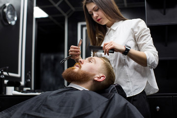 Obraz na płótnie Canvas stylist girl shaves beard man in Barbershop