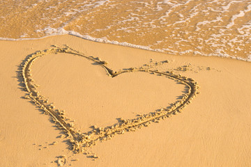 Heart on a wet sand. Painted heart. Season of travel. Summer trips to the sea. Concept of leisure and travel. Waves wash away the painted heart on the sand
