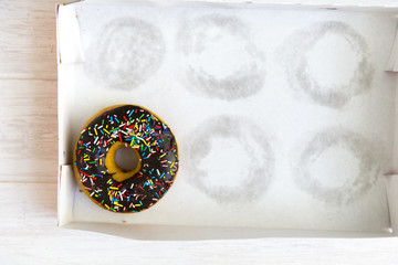 Empty cakes box with only one tempting and delicious donut with toppings left in unhealthy...