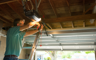 Professional automatic garage door opener repair service technician man working on a ladder at a home residential location making adjustments and fixing it while installing it. - 144646378