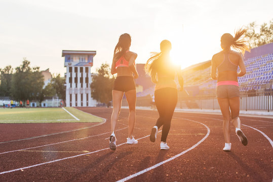 Rear View Of Women Athletes Running Together In Stadium.