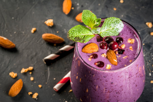 Healthy food. Dietary breakfast, snack. Berry smoothies with granola, black currant, blueberries and nuts almonds, decorated with mint. On a dark concrete table with ingredients, copy space