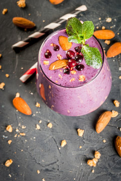 Healthy food. Dietary breakfast, snack. Berry smoothies with granola, black currant, blueberries and nuts almonds, decorated with mint. On a dark concrete table with ingredients, copy space