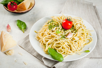 Italian cuisine, lunch or dinner for one. Pesto pasta. Spaghetti with pesto, basil leaves, garlic, parmesan cheese and cherry tomatoes. One portion. On a white stone table. Copy space