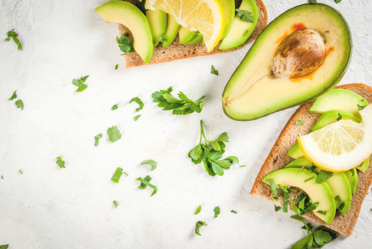Healthy diet food. Spring meal. Sandwiches of black bread with avocado, lemon and greens. With ingredients on cutting board on white stone table