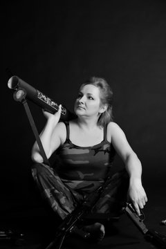 A middle aged, white, woman holds a RPG18 Mukha grenade launcher, with weapon around against black