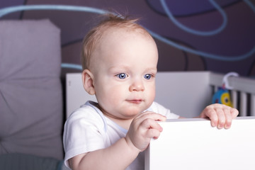 Satisfied and calm baby boy in his bed. An infant kid staying in a crib