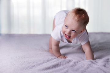 The boy with tongue hanging out doing his first steps. Open-eyed infant kid on the bed trying to toddle. Copy space