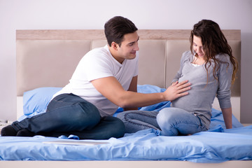 Young family with pregnant wife expecting baby in bed