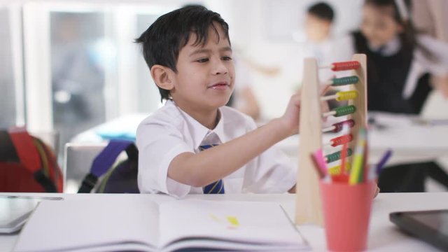 Young school children in class with little boy using abacus & computer tablet