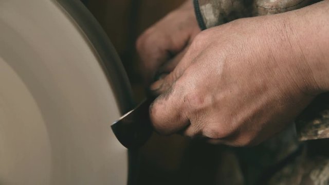 Closeup of hands grinding metal knife at grindstone machine in traditional smithy