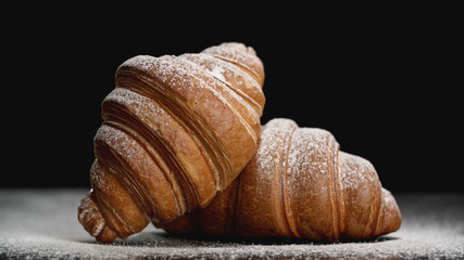 Delicious croissants with powdered sugar on black background