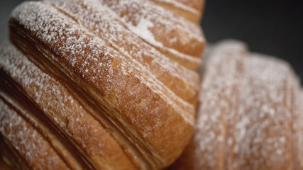 Delicious croissants with powdered sugar on black background