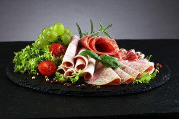 Food tray with delicious salami, pieces of sliced ham, sausage, tomatoes, salad and vegetable - Meat platter with selection