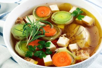 Broth with carrots, onions various fresh vegetables in a pot - colorful fresh clear spring soup. Rural kitchen scenery vegetarian bouillon or stock