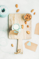 Naklejka na ściany i meble Fresh vegan dairy-free almond milk in glass bottle with craft paper label with copy space on serving wooden board over light grey background, top view. Vegan, raw, clean eating, diet food concept