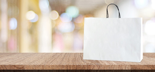 White shopping bag on wooden table over blurred store background, business, template, product...