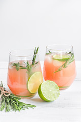 sliced lime, rosemary and natural juice in glass on white table background