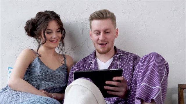 Close up of young couple watching videos on tablet and talking in bed together. Online shopping and entertainment at home.