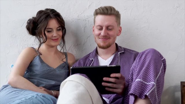 Close up of young couple watching videos on tablet. Loving couple who are dressed in homemade pajamas smile and enjoy a joint day off.