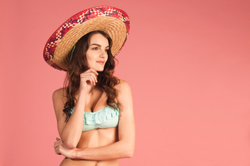 young happy beautiful female in bikini and straw hat looking right on pink background