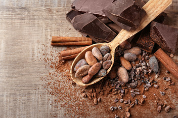 Spoon with cocoa beans and chocolate on wooden background