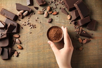 Woman holding bowl with aromatic cocoa powder and pieces of chocolate on wooden background