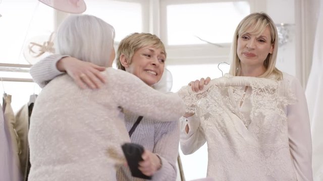 Bride to be shopping for her wedding dress with emotional mother & grandmother