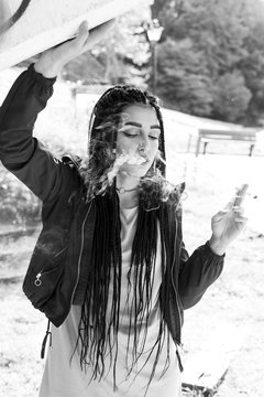 Braided young woman smoking outdoors. With african braids, pierced fashion woman. Converted to black and white, grain added.