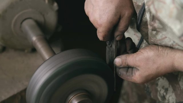 Closeup of hands grinding metal knife at grindstone machine in traditional smithy