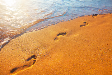 beach, wave and footprints at sunset time