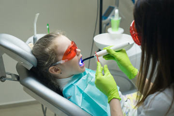 close up view of small girl patient at the dentist. Doctor is making dental fillings with ultraviolet light. Girl is wearing protective glasses.