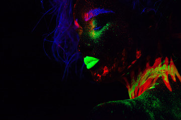 Beautiful extraterrestrial model woman with blue hair and green lips in neon light. It is close portrait of beautiful model with fluorescent make-up, Art design of female posing in UV with colorful