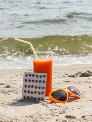 Medical pills, carrot juice and sunglasses on sand at beach, vitamin A and beautiful, lasting tan