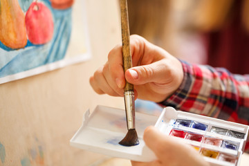 Obraz premium Artist mixes watercolors on a plastic palette. Hand and brush close-up. Brush of a hair pony.