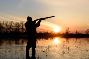 Papier Peint photo autocollant Chasser Silhouette d& 39 un chasseur au coucher du soleil dans l& 39 eau avec une arme à feu.
