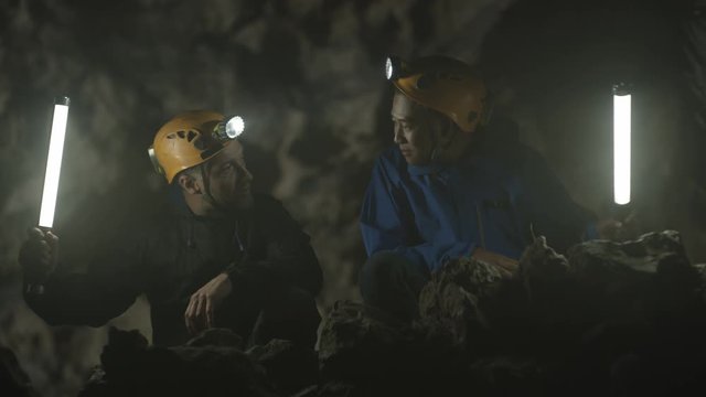  Spelunkers exploring underground cave, discussing rock formation
