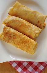 Three Stuffed pancakes on a white rectangular plate On a checkered red white  napkin