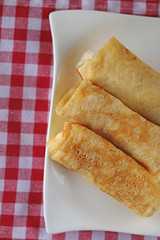 Three Stuffed pancakes on a white  plate On a checkered red white cotton napkin