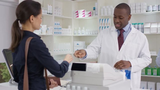  Friendly pharmacy worker serving customers & taking payment at the till