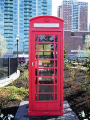 Imitation classic British London red phone booth in a park with modern highrise building in the background