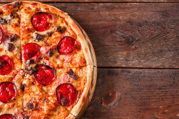 Délicieuse pizza fraîche avec salami, jambon, fromage, viande et bacon servie sur une table rustique en bois, mise à plat. Fond sombre avec espace libre. Cuisine traditionnelle italienne.