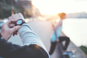 Couple of athletes practicing sport on the street. Man tracking time using his arm watch. Young woman doing step exercise near the river